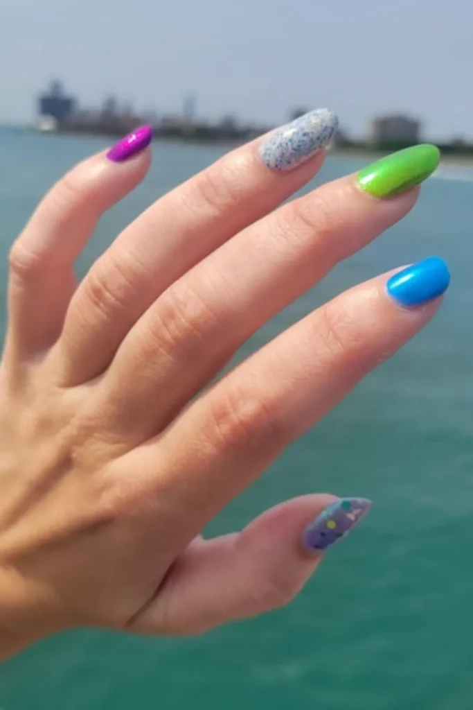August Nails Ideas featuring a colorful mix-and-match manicure with magenta, neon green, bright blue, glitter, and butterfly accent nails