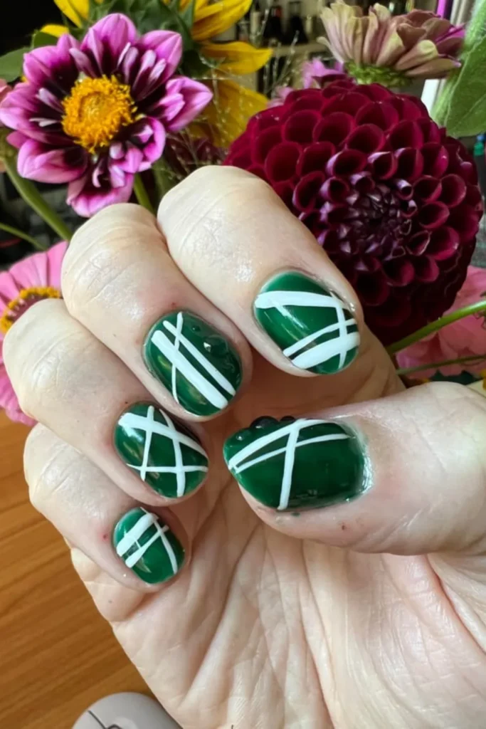 August Nails Ideas showcasing deep forest green polish with white geometric grid lines and 3D clear water droplet accents