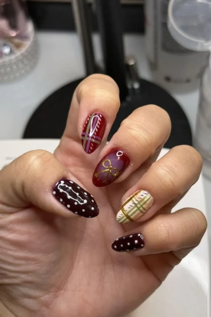 Burgundy and plaid patterned nail design with a gold bow accent for fall transition nails ideas