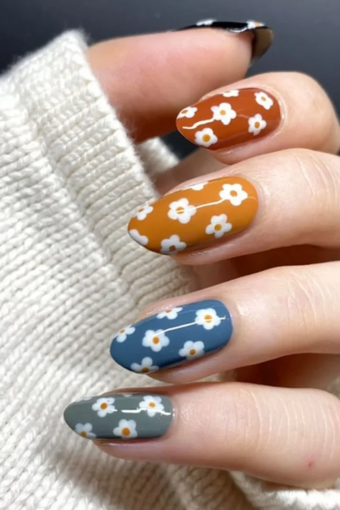 Earthy burnt orange, mustard yellow, and slate blue nails with simple white retro daisy patterns for fall transition nails ideas