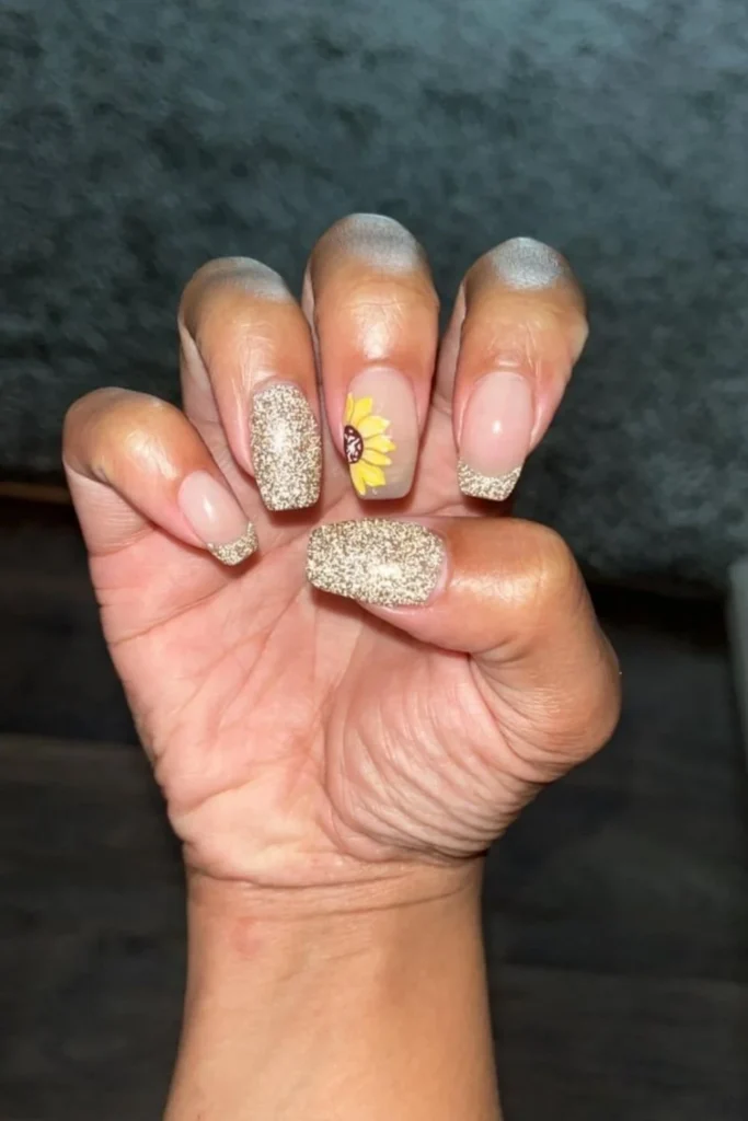 Gold glitter accent manicure featuring a yellow sunflower art detail for fall transition nails ideas