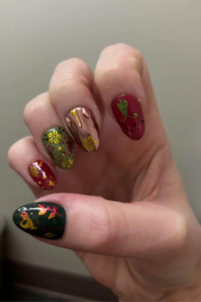 Rich jewel-toned green and cranberry red manicured nails with intricate gold floral folk art detailing for fall transition nails ideas