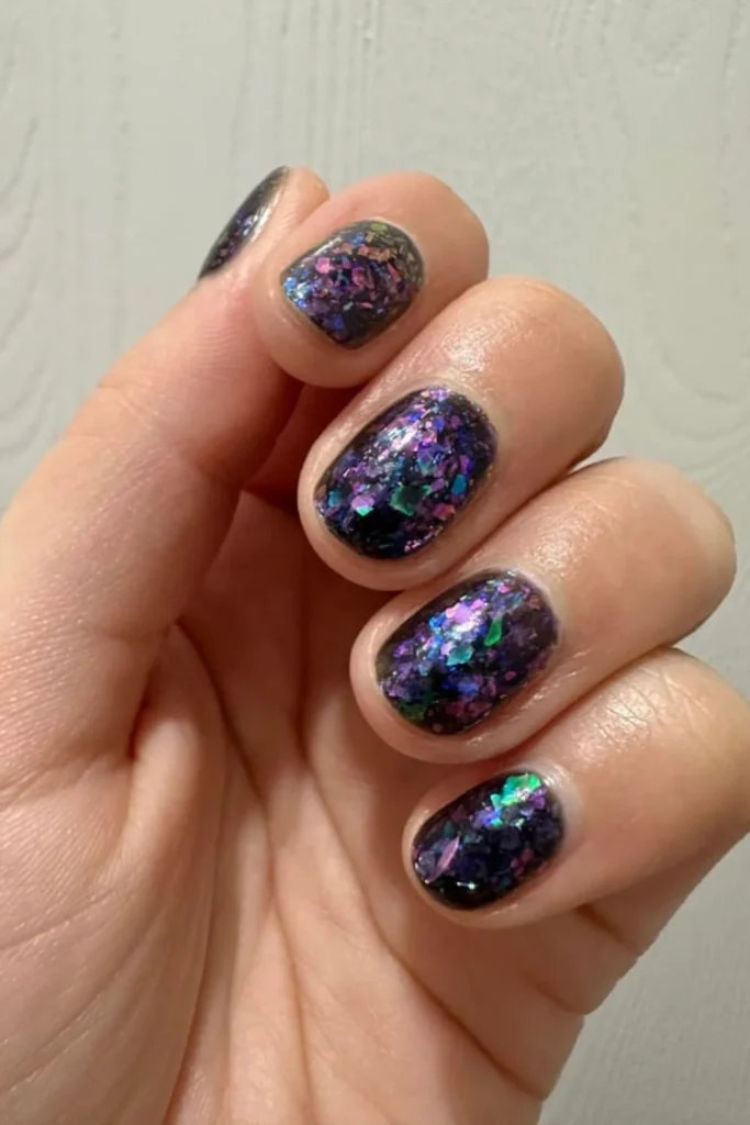 Moody September nails ideas on short rounded nails covered in dark purple polish with multidimensional iridescent blue and green flakies
